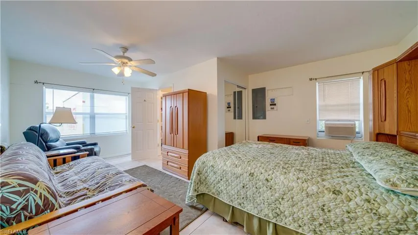 Tiled bedroom featuring electric panel, ceiling fan, cooling unit, and multiple windows