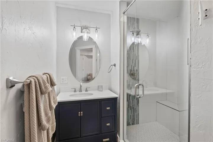 Bathroom featuring a stall shower, a textured wall, and vanity