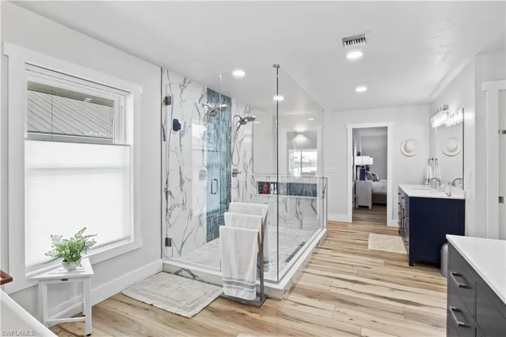 Ensuite bathroom with wood finished floors, vanity, visible vents, and a healthy amount of sunlight