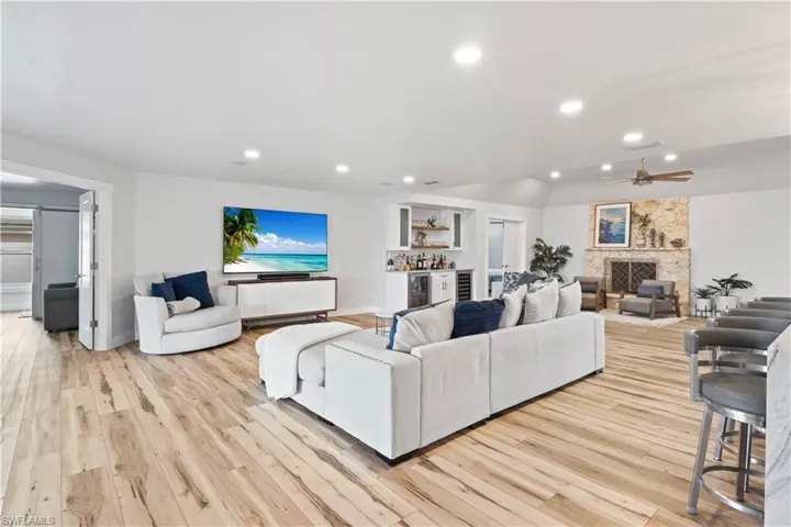 Living room featuring a fireplace, a dry bar, recessed lighting, light wood-style floors, and vaulted ceiling