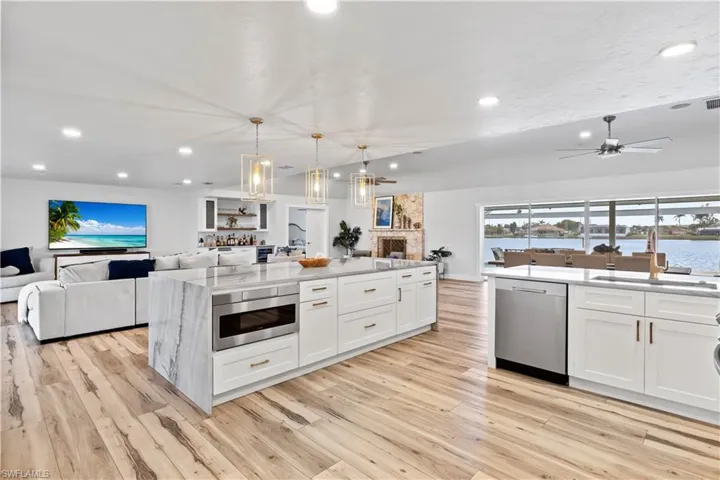 Kitchen featuring light wood-style flooring, appliances with stainless steel finishes, open floor plan, white cabinetry, and a sink