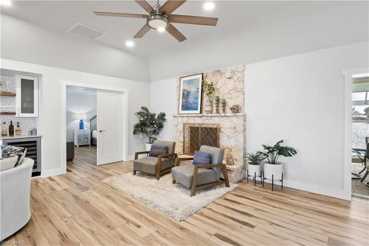 Sitting room with wine cooler, ceiling fan, a stone fireplace, a bar, and light wood-type flooring