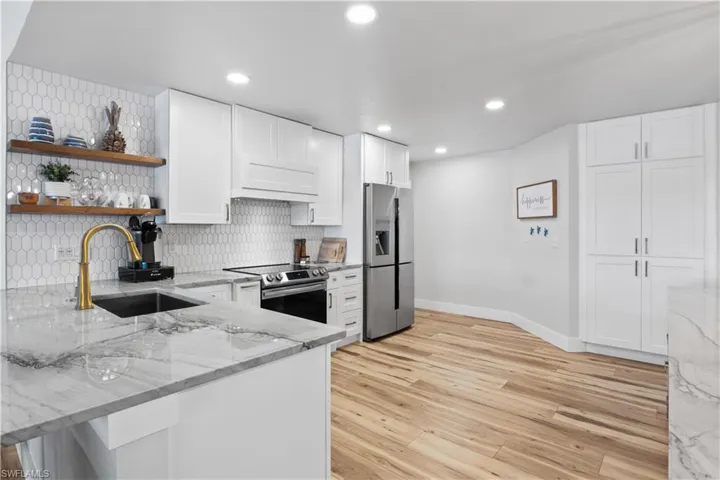 Kitchen with white cabinets, a sink, stainless steel appliances, open shelves, and backsplash