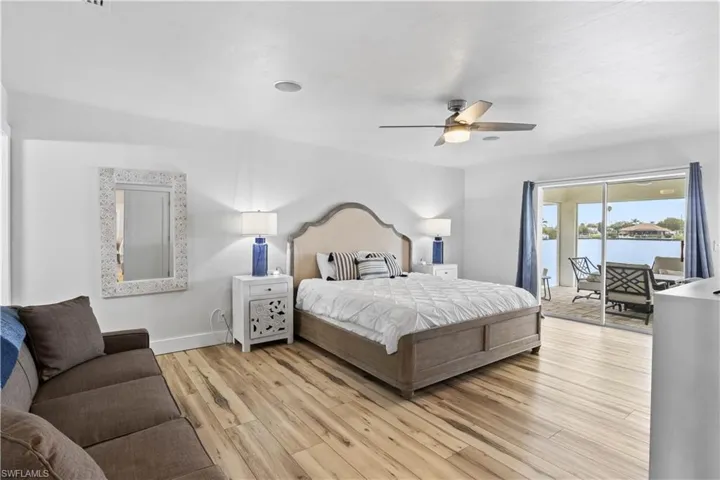 Bedroom featuring access to exterior, a water view, light wood-style floors, ceiling fan, and baseboards