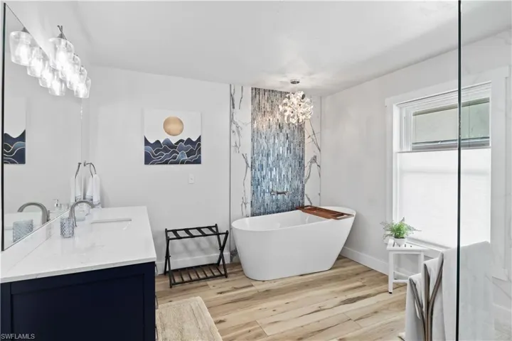 Bathroom featuring double vanity, a soaking tub, a sink, wood finished floors, and baseboards