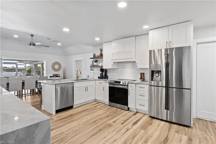 Kitchen featuring appliances with stainless steel finishes, light wood-style floors, white cabinetry, a sink, and a peninsula