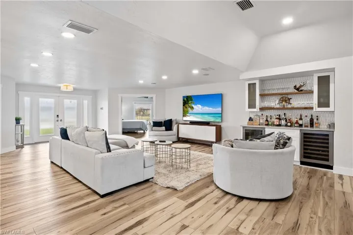 Living area featuring french doors, a bar, visible vents, and light wood-style floors