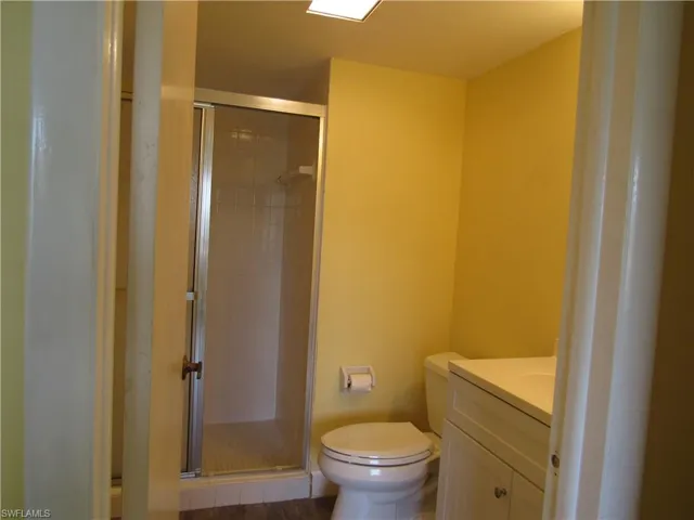 Bathroom featuring a shower with door, toilet, and vanity