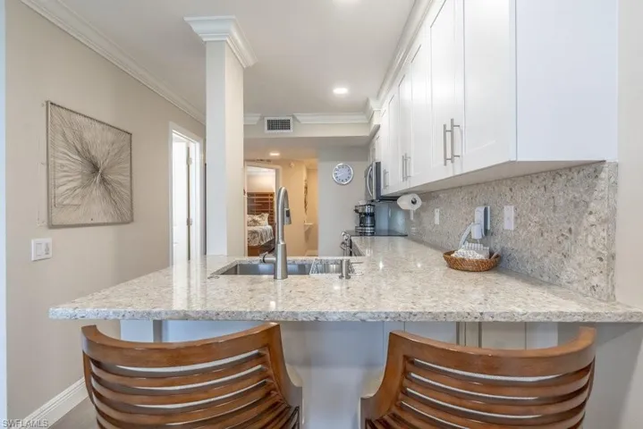 Kitchen featuring a sink, white cabinetry, a peninsula, tasteful backsplash, and light stone countertops