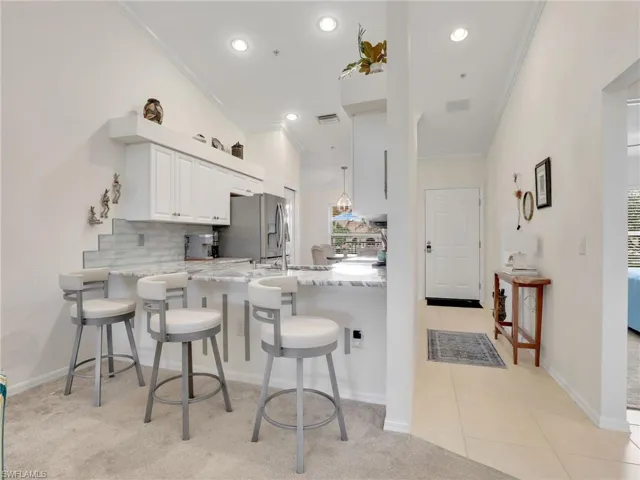 Kitchen featuring white cabinets, crown molding, light stone counters, kitchen peninsula, and a breakfast bar area
