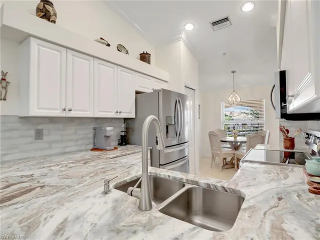 Kitchen with decorative backsplash, stainless steel refrigerator with ice dispenser, light stone counters, pendant lighting, and white cabinets
