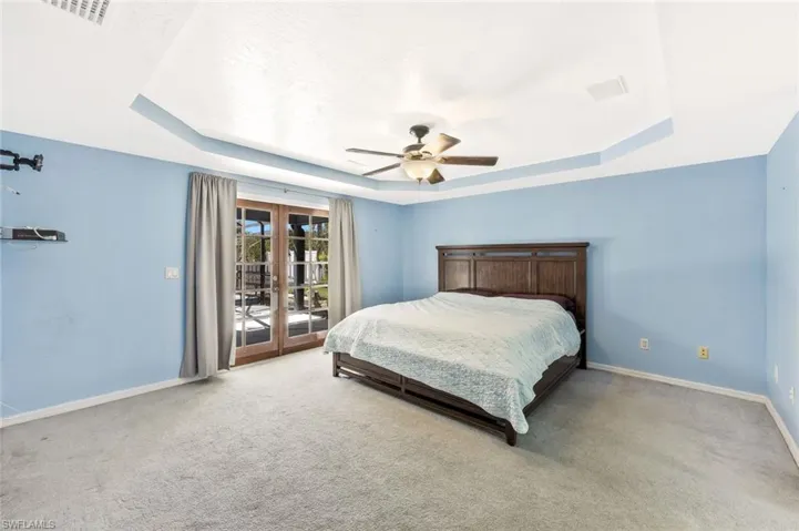 Bedroom featuring french doors, access to exterior, a raised ceiling, light colored carpet, and a ceiling fan