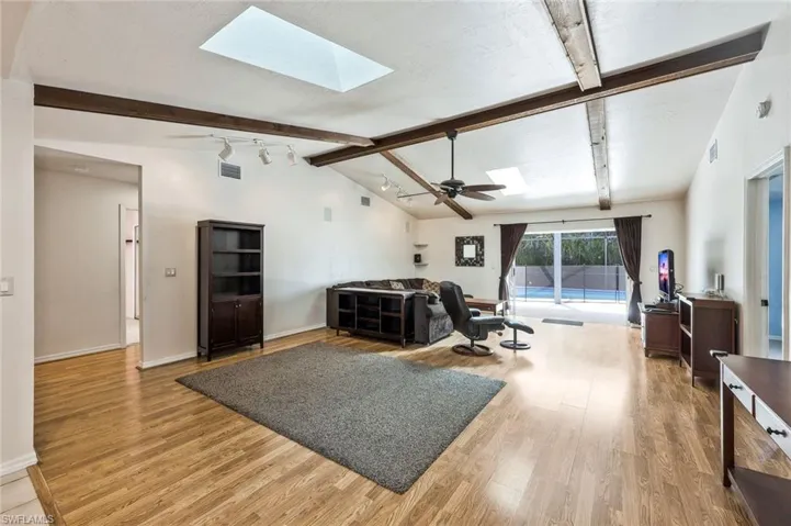 Living room featuring a skylight, beamed ceiling, light wood-type flooring, a ceiling fan, and rail lighting