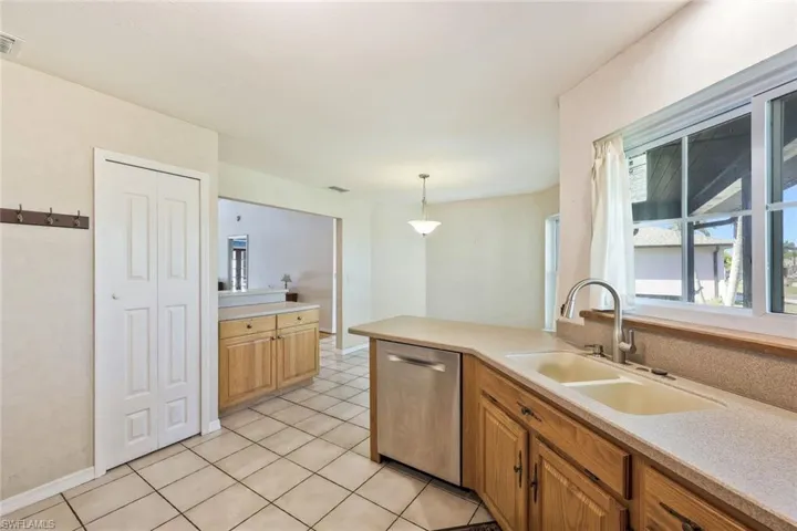 Kitchen with decorative light fixtures, dishwasher, a peninsula, and light tile patterned floors