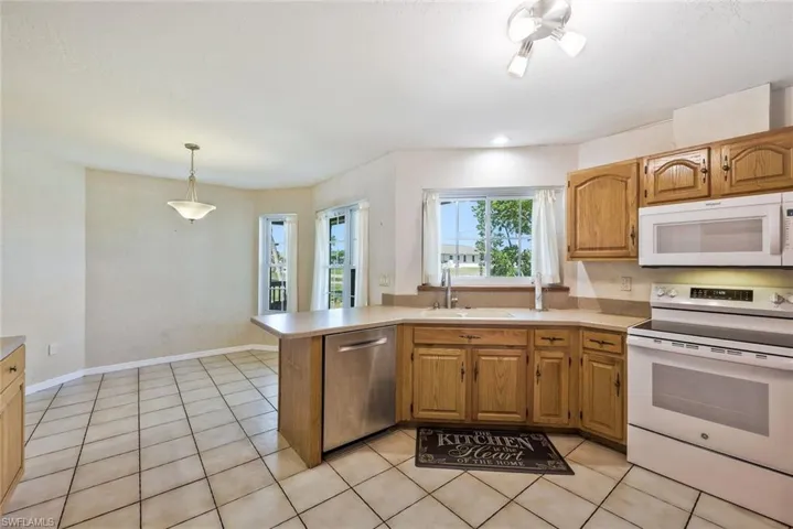 Kitchen with white appliances, light countertops, a peninsula, wood finish cabinetry, and pendant lighting