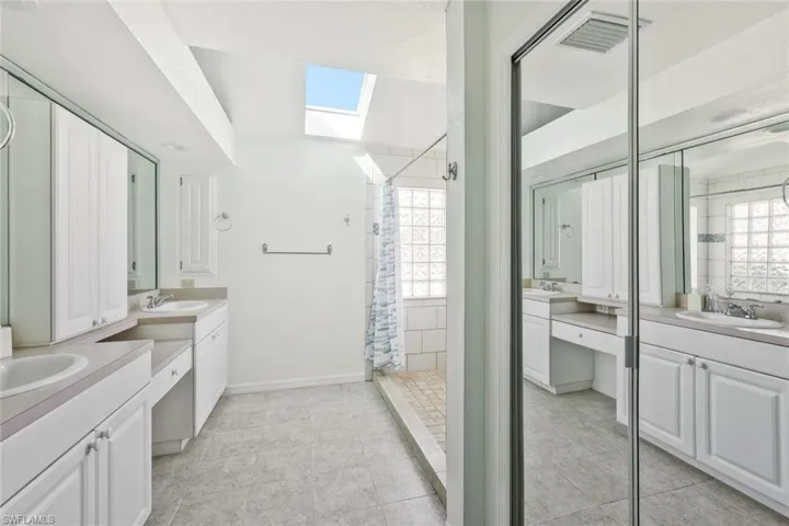 Bathroom with two vanities, a skylight, a shower stall, and light tile patterned flooring