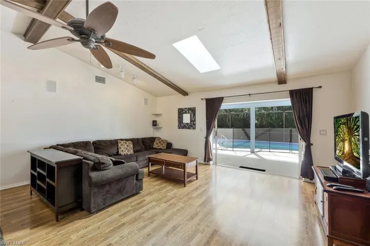 Living area featuring a skylight, vaulted ceiling with beams, a ceiling fan, and light wood-style floors
