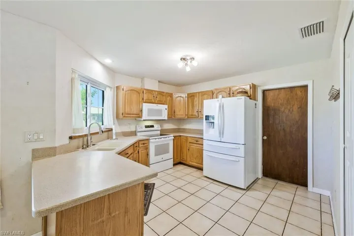 Kitchen with light countertops, white appliances, a peninsula, light tile patterned floors, and recessed lighting