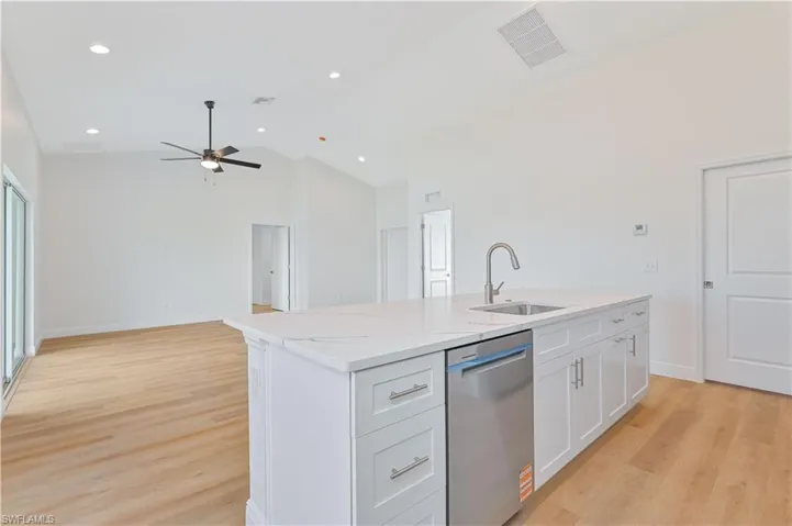 Kitchen with stainless steel dishwasher, a sink, ceiling fan, a center island with sink, and white cabinetry