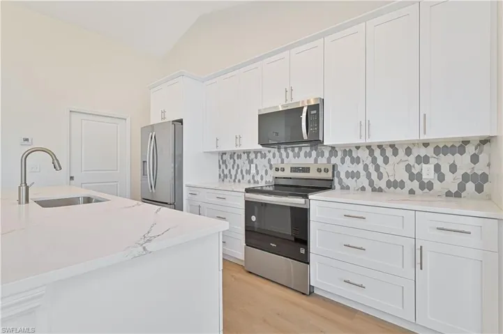 Kitchen featuring stainless steel appliances, a sink, white cabinets, tasteful backsplash, and lofted ceiling