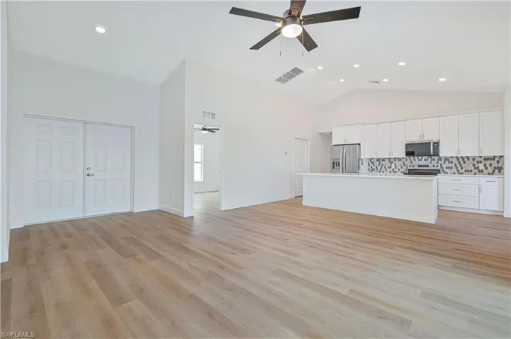 Unfurnished living room with ceiling fan, high vaulted ceiling, light wood finished floors, and recessed lighting
