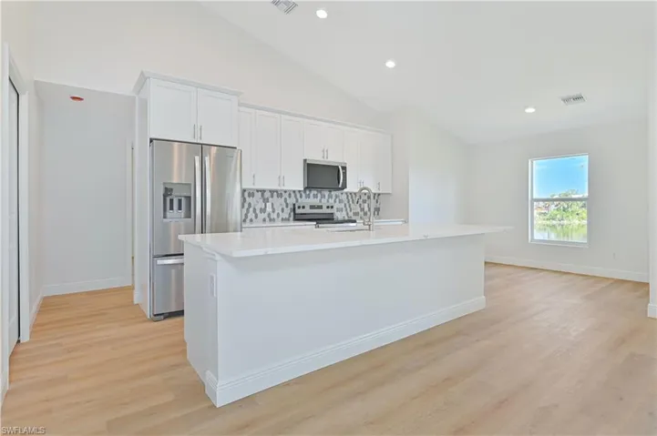 Kitchen with appliances with stainless steel finishes, backsplash, a kitchen island with sink, vaulted ceiling, and light countertops