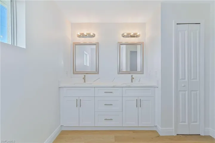 Bathroom with wood finished floors, double vanity, baseboards, and a closet