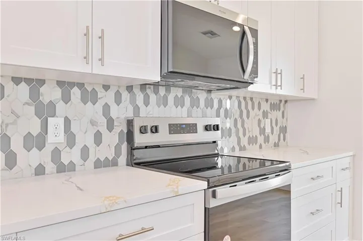 Kitchen featuring appliances with stainless steel finishes, backsplash, white cabinets, light stone counters, and wood finished floors
