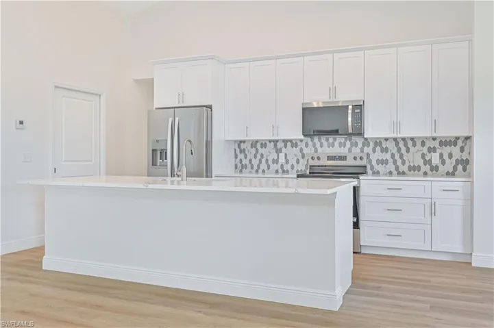 Kitchen with appliances with stainless steel finishes, a kitchen island with sink, light countertops, decorative backsplash, and white cabinetry