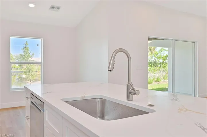 Kitchen with a sink, stainless steel dishwasher, light stone counters, white cabinetry, and light wood-style flooring