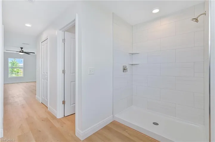 Bathroom with tiled shower, wood finished floors, baseboards, recessed lighting, and a ceiling fan