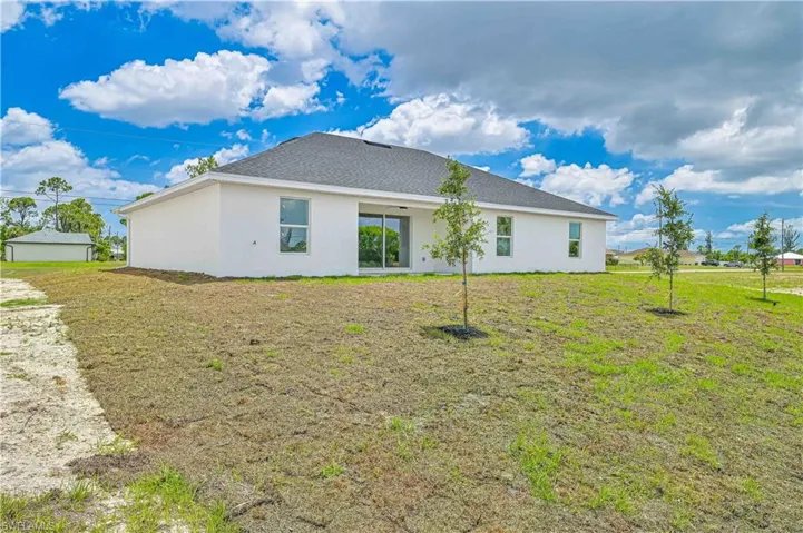 Back of property featuring stucco siding, a lawn, and a shingled roof
