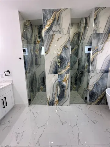 Full bath featuring a marble finish shower, vanity, a freestanding bath, and stone wall