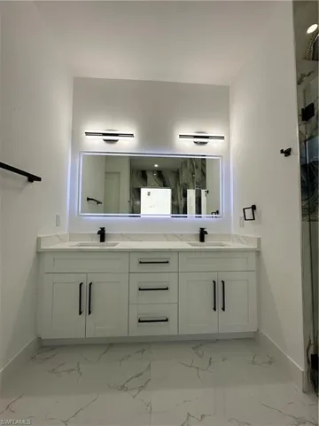 Bathroom featuring double vanity, a marble finish shower, and light marble finish floors