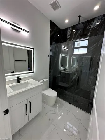 Full bath featuring vanity, a marble finish shower, recessed lighting, and light marble finish flooring