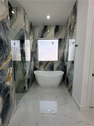 Full bathroom with stone wall, a freestanding tub, and a marble finish shower
