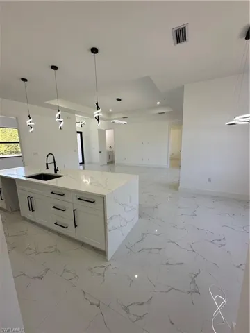 Kitchen featuring pendant lighting, a kitchen island with sink, open floor plan, white cabinetry, and light stone countertops