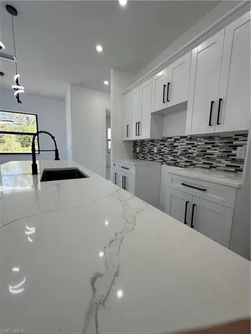 Kitchen with light stone counters, white cabinets, hanging light fixtures, and tasteful backsplash