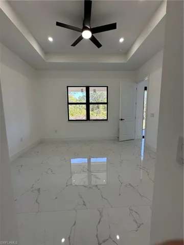 Spare room with a tray ceiling, ceiling fan, recessed lighting, and light marble finish floors