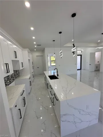 Kitchen featuring a large island with sink, light stone countertops, white cabinetry, hanging light fixtures, and open floor plan