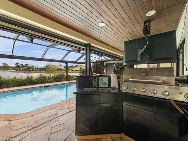View of swimming pool featuring a lanai, area for grilling, sink, a water view, and a patio area