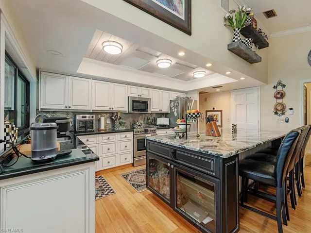 Kitchen with crown molding, appliances with stainless steel finishes, white cabinetry, a tray ceiling, and a kitchen island