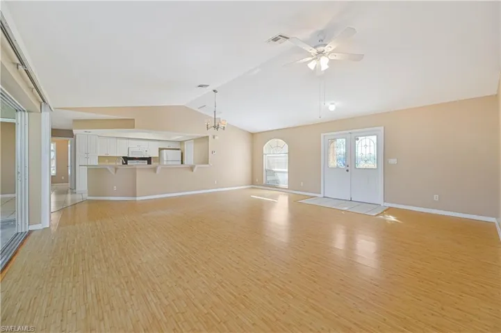 Unfurnished living room featuring french doors, lofted ceiling, ceiling fan with notable chandelier, and light hardwood / wood-style flooring