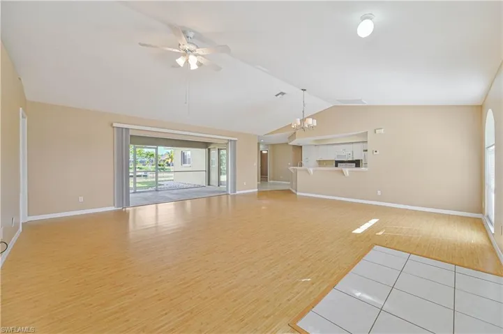 Unfurnished living room with vaulted ceiling, ceiling fan with notable chandelier, and light wood-type flooring