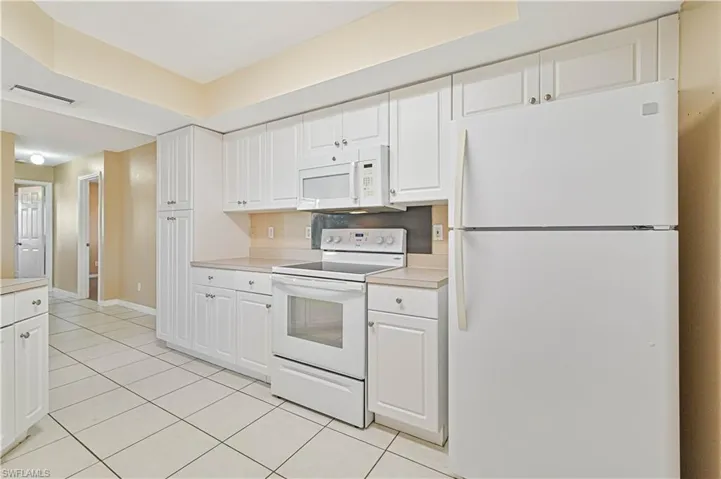 Kitchen featuring light tile patterned flooring, white cabinets, and white appliances