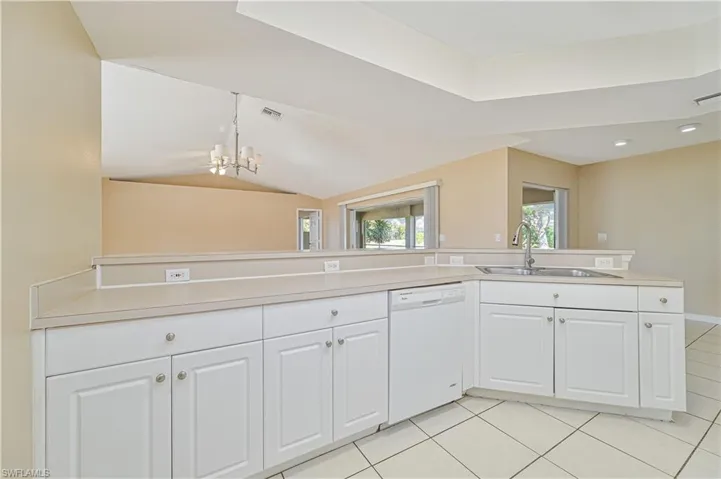 Kitchen with lofted ceiling, sink, white cabinetry, light tile patterned floors, and dishwasher
