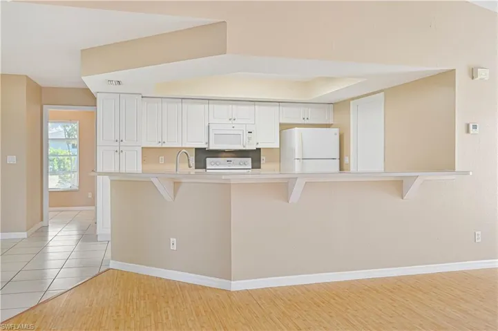 Kitchen with white cabinetry, white appliances, a kitchen bar, and light tile patterned floors