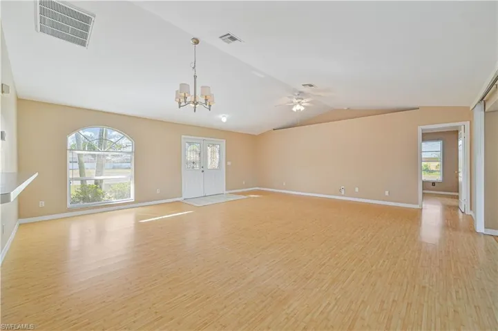 Unfurnished living room with lofted ceiling, plenty of natural light, ceiling fan with notable chandelier, and light hardwood / wood-style flooring