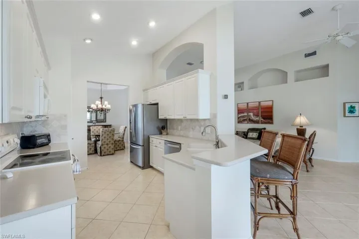 Kitchen with vaulted ceiling, light tile patterned floors, white cabinetry, appliances with stainless steel finishes, and a kitchen breakfast bar