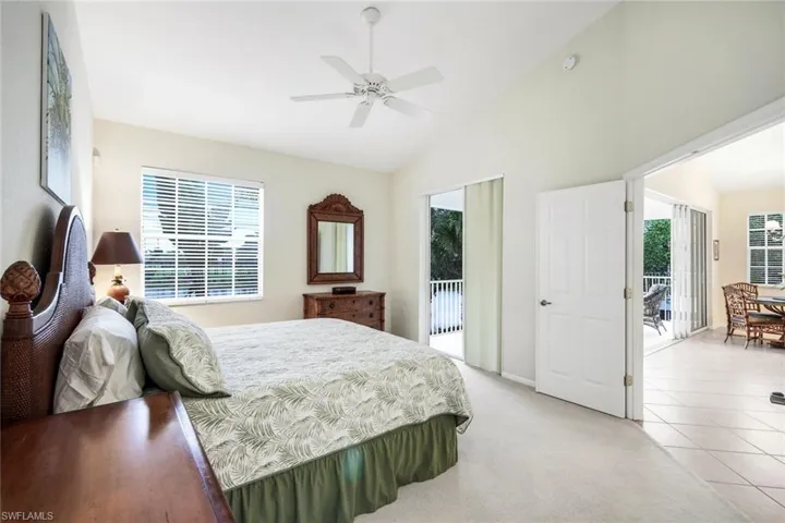 Bedroom featuring access to outside, vaulted ceiling, multiple windows, light colored carpet, and a ceiling fan